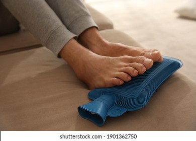 Man Warming Feet With Hot Water Bottle On Sofa, Closeup