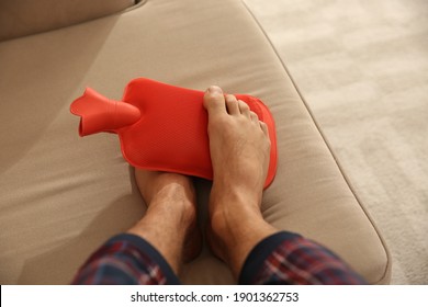 Man Warming Feet With Hot Water Bottle On Sofa, Closeup