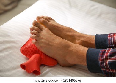 Man Warming Feet With Hot Water Bottle On Bed, Closeup