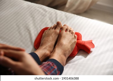 Man Warming Feet With Hot Water Bottle On Bed, Closeup