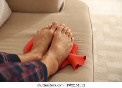 Man Warming Feet With Hot Water Bottle On Sofa, Closeup