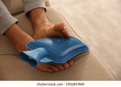 Man Warming Feet With Hot Water Bottle On Sofa, Closeup