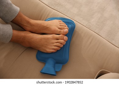 Man Warming Feet With Hot Water Bottle On Sofa, Closeup