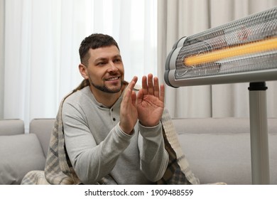 Man Warming Hands Near Electric Infrared Heater At Home