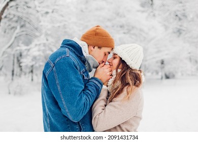 Man Warming Hands Of Woman With His Breath In Snowy Cold Winter Park. Loving Couple Walking Outdoors During Frosty Weather