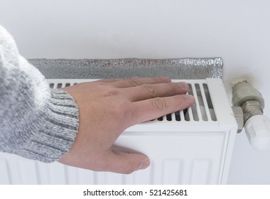 A Man Warms His Hand On A Central Heating Radiator.