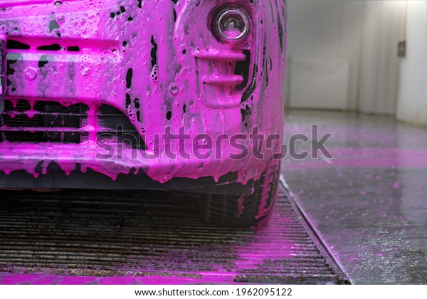 a man wash a car with pink foam and water at a
self-service car wash
