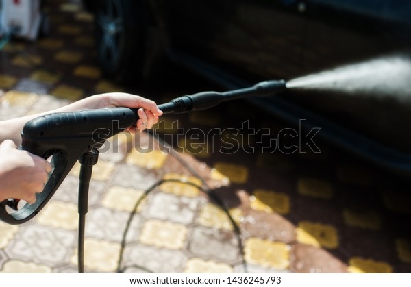 A man washes a black car from a hose with\
high-pressure water near the\
garage