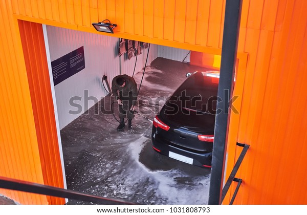 a man washes a car in a box contactless car wash\
self-service with a water gun in the manual self-service washing\
station. top view