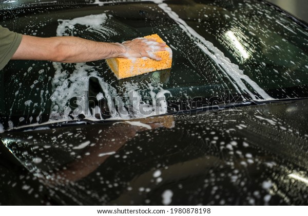 a\
man washes a car with a sponge in foam at a car\
wash