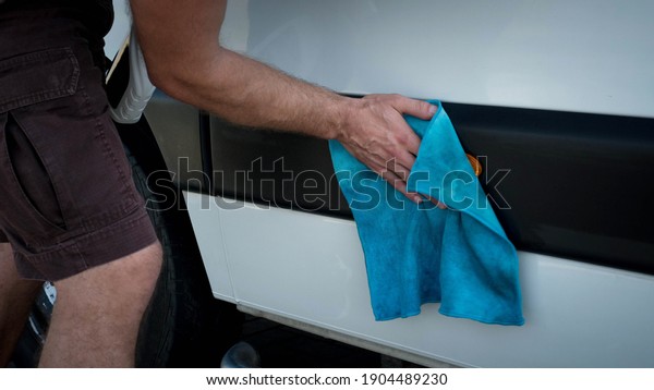 A man washes a\
cargo car, a man rubs a car with a rag, a car wash worker washes\
the car with a detergent.