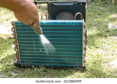 A Man Washes And Cleans The Condenser Coil Of An Old Window Type Air Conditioning Unit On The Ground With A High Pressure Hose. Cleaning An AC Unit In The Yard.