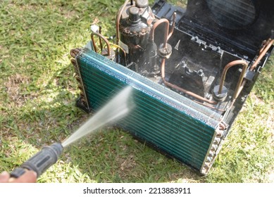 A Man Washes And Cleans The Condenser Coil Of An Old Window Type Air Conditioning Unit On The Ground With A High Pressure Hose. Cleaning An AC Unit In The Yard.