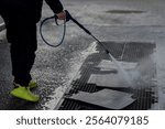 A man washes dirty rubber carpets from cars at a paid car wash using a special hose before washing the car. Washing a car mat with a high pressure washer. Hand holding a dirty black rubber car mat.