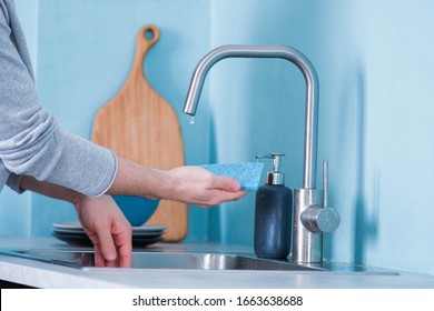 A man washes dishes in the kitchen with a blue eco sponge in the kitchen with blue walls. modern interior