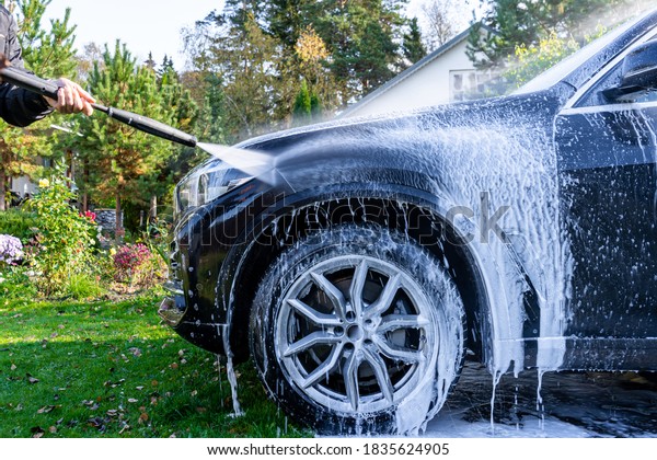 A man washes his car at home in the\
garden using a high-pressure washer with\
foam