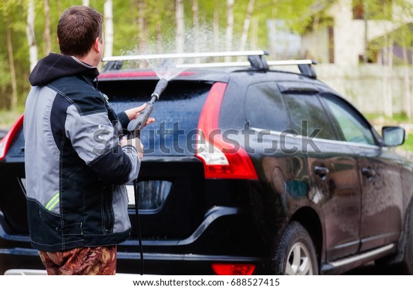 A man washes his car in\
the yard