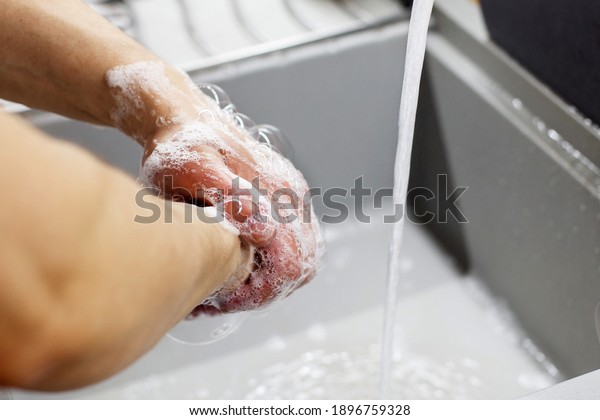 A man\
washes his hands with soap under the tap under running water\
close-up. Health, cleanliness and hygiene\
concept.