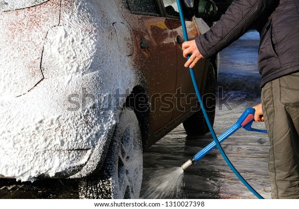 Man washes his orange car at car\
wash. Cleaning with soap suds at self-service car\
wash.