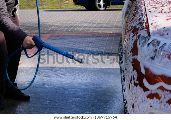 Man washes his orange car at car wash.\
Cleaning with soapy at self-service car wash. Soapy water runs\
down. Male hand and car body close\
up.