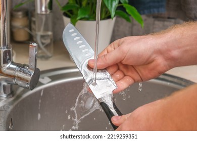 A man washes a sharp steel dirty kitchen knife with a sponge with detergent in the kitchen sink under running water. Gentle hand washing of the kitchen knife. Cleaning of dirty sharp metal products.