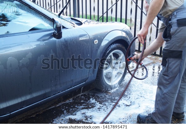 A man is\
washing black Cabriolet car in open air. A man spends his weaken to\
wash his lovely car in front of garage. He is cleaning wheel of car\
with sponge and bubble soap 