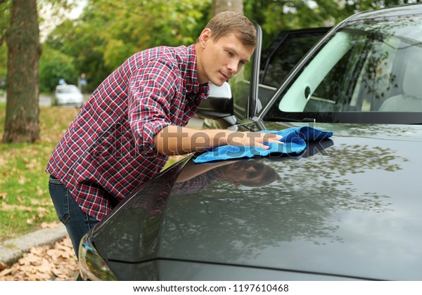 Man washing car hood\
with rag outdoors