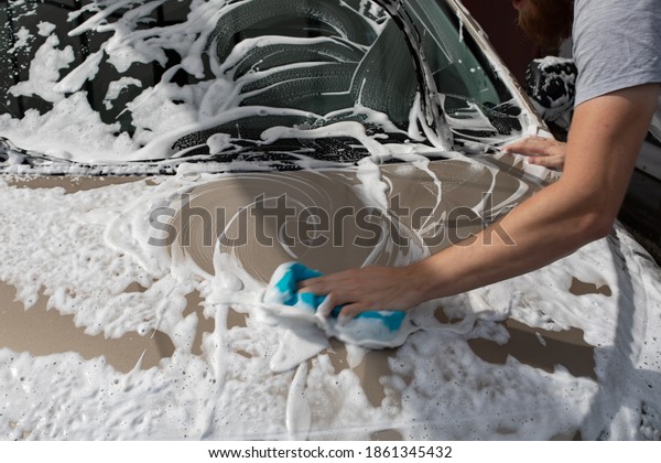 Man washing car hood with\
washcloth and shampoo, auto covered with foam, car wash\
service