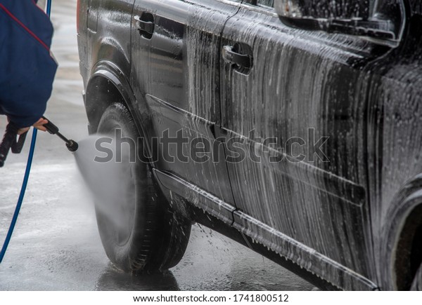 A man is washing a\
car at self service car wash. High pressure vehicle washer machine\
sprays foam.