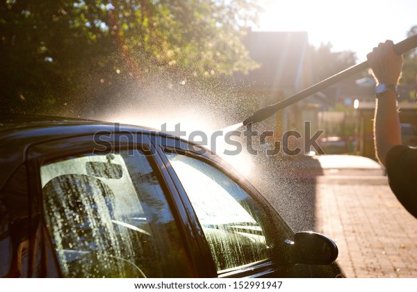 man\
washing car in sunshine with high pressure\
washer