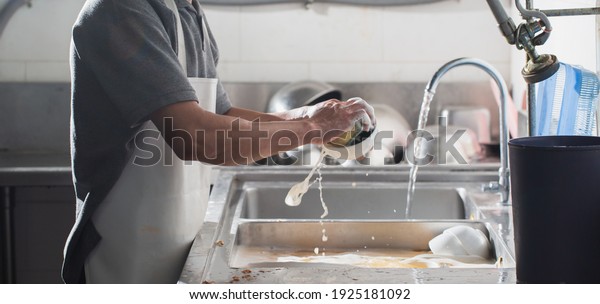 Man washing dish in sink at\
restaurant.People are washing the dishes too Cleaning\
solution