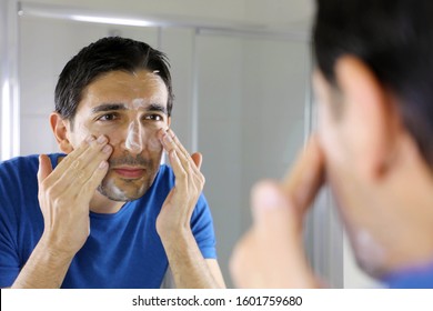 Man Washing Face With Facial Cleanser Face Wash Soap Looking At Mirror In Bathroom At Home. Men Skin Care Concept.