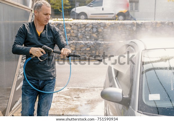 Man washing his car with\
using a high pressure water jet. man washing his car with\
compression water. Man washing his car in a self-service car wash\
station
