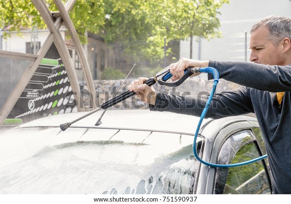 Man washing his car with\
using a high pressure water jet. man washing his car with\
compression water. Man washing his car in a self-service car wash\
station