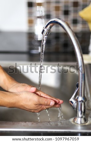 A man washing his hands at a faucet sink and water tab.