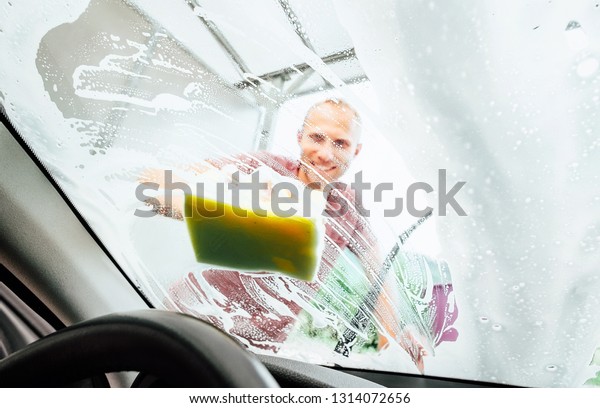Man washing his new car windshield window inside the\
car camera view