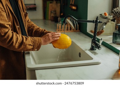 Man washing melon under tap at kitchen  - Powered by Shutterstock