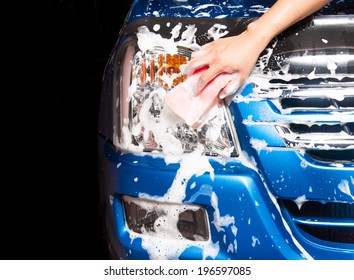 man washing a soapy blue car with a pink sponge.