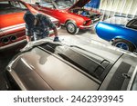 Man washing vintage car hood in garage. Classic vehicles theme