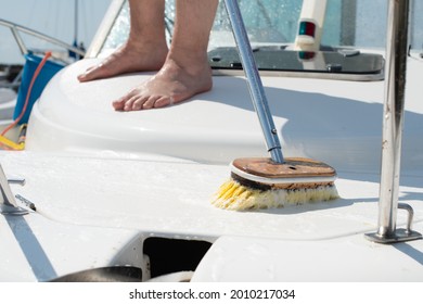Man washing white boat with brush and pressure water system at pier. Yacht maintenance concept.