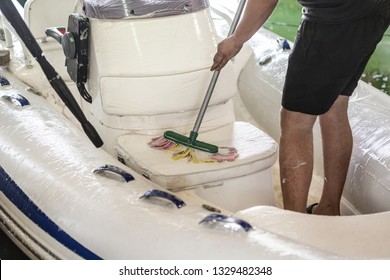 Man washing white inflatable boat with brush and pressure water system at garage. Ship service and seasonal maintenance concept
