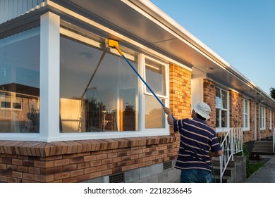 Man Washing Windows Of An Empty House With Long Pole And Brush. Home Refurbishment Project In Auckland. 