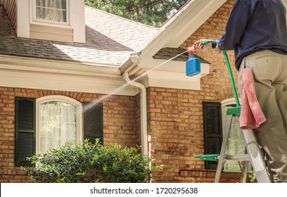 Man Washing Windows Of The House With A Power Wash Sprayer. Cleaning Service Using A High Pressure Water Jet To Clean The Facade Of Residential Building. Spring Cleaning With Hose And Pressure Washer.