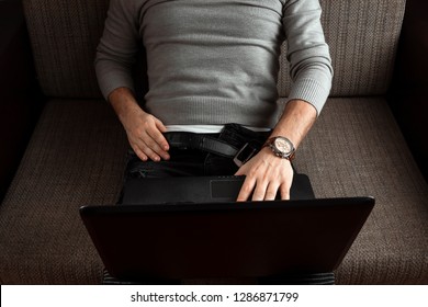 A man watches an adult video in a laptop sitting on the couch. Concept porn videos, anonism, desire, loneliness.