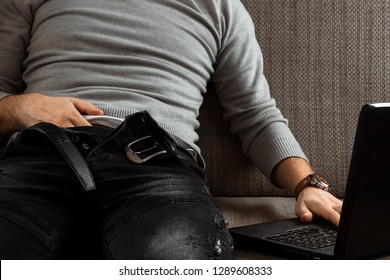 A Man Watches An Adult Video On A Laptop While Sitting On The Couch. The Concept Of Porn, Masturbation, Male Needs, Pervert, Lust, Desire, Loneliness.