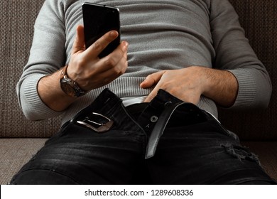 A man watches an adult video on a phone while sitting on a couch. The concept of porn, masturbation, male needs, pervert, lust, desire, loneliness.