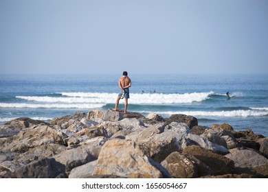 A man watches quietly from the rocks as they surf on a sunny summer day at the beach - Powered by Shutterstock