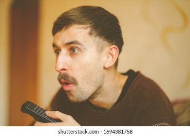 A Man Watches TV. A Man With A Remote Control In His Hands. Serious Man With A Remote Control In His Hands. Vintage Photo Processing.