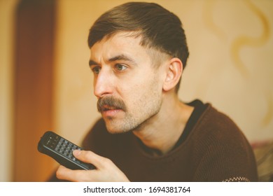 A Man Watches TV. A Man With A Remote Control In His Hands. Serious Man With A Remote Control In His Hands. Vintage Photo Processing.