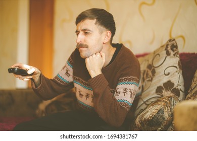 A Man Watches TV. A Man With A Remote Control In His Hands. Serious Man With A Remote Control In His Hands. Vintage Photo Processing.